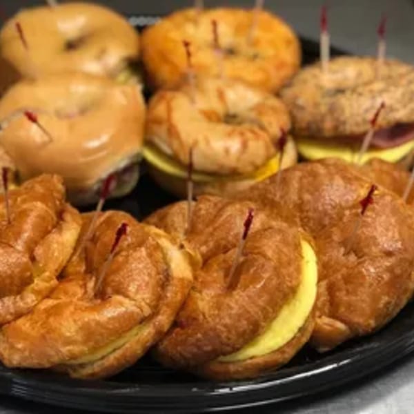 A platter of New York Bagel Company's bagel and croissant breakfast sandwiches with toothpicks.