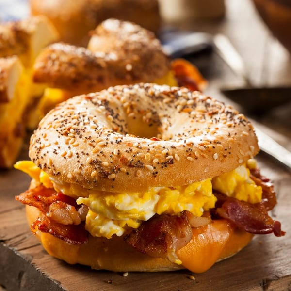 Everything bagel with scrambled eggs, crispy bacon, and melted cheese on a wooden board.