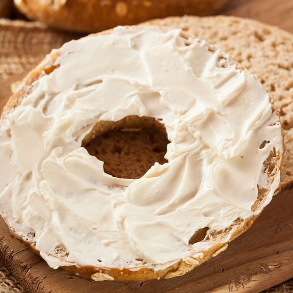 A New York Bagel Company whole wheat bagel, sliced and generously spread with cream cheese.
