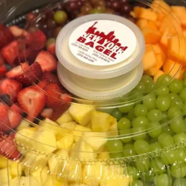 A fruit platter with strawberries, pineapple, cantaloupe, and grapes, with a New York Bagel cream cheese container.