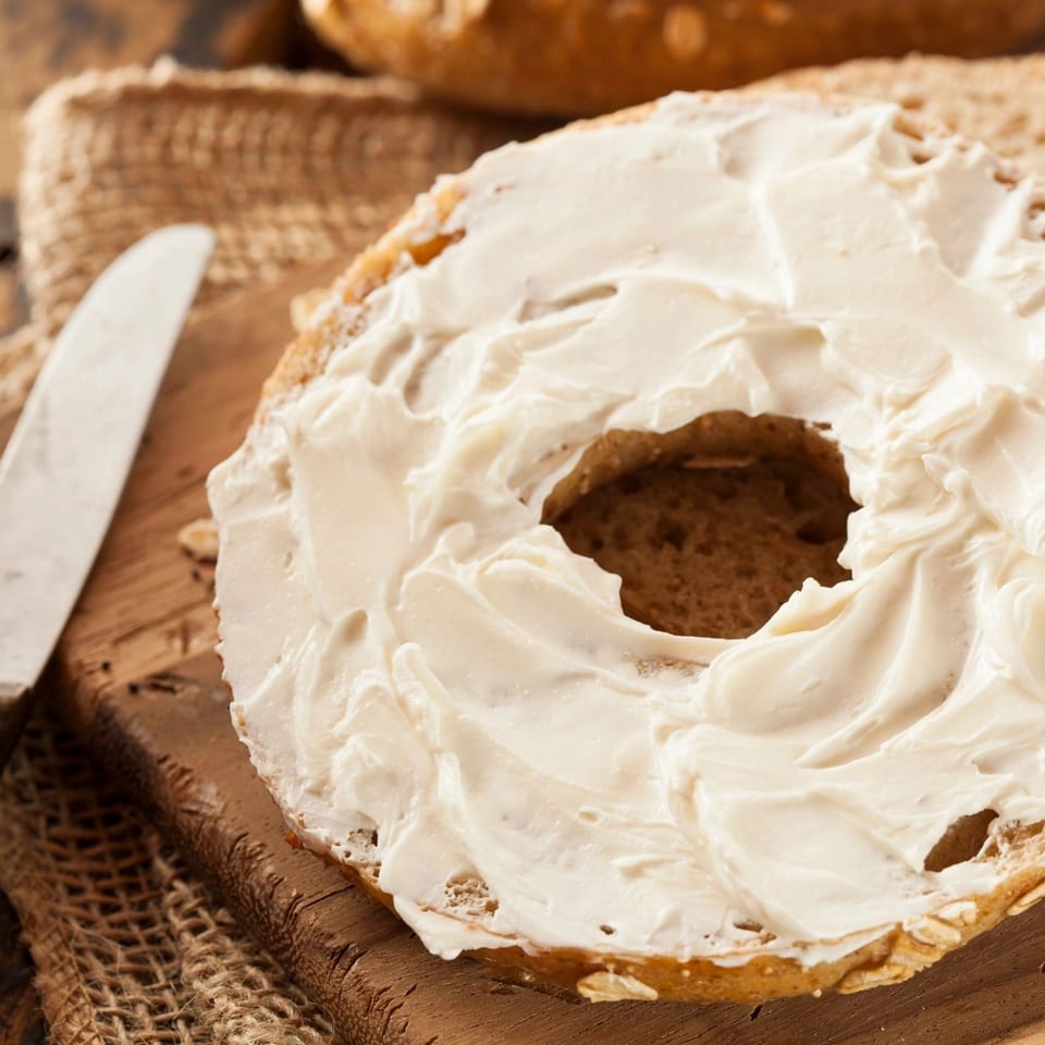 New York Bagel Company's bagel with cream cheese on a wooden board with a knife.