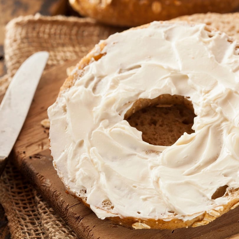 New York Bagel Company's bagel with cream cheese on a wooden board with a knife.