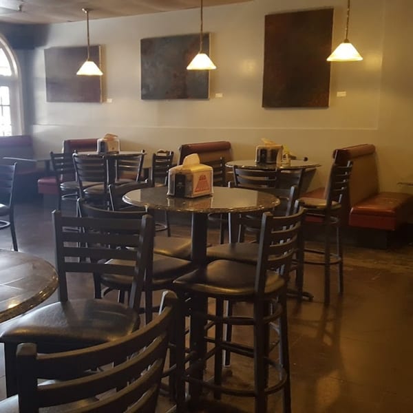 Interior of New York Bagel Company with empty tables, chairs, and booths under pendant lights.