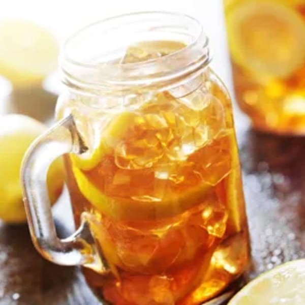 Iced tea with lemon slices and ice in a mason jar, with lemons in the background.
