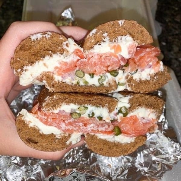 A New York Bagel Company bagel with lox, cream cheese, and capers, held over foil.