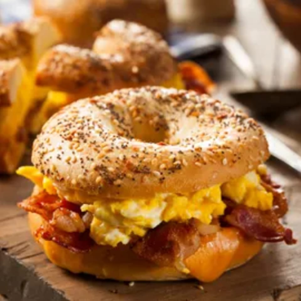 Everything bagel with scrambled eggs, bacon, and melted cheese on a wooden board.