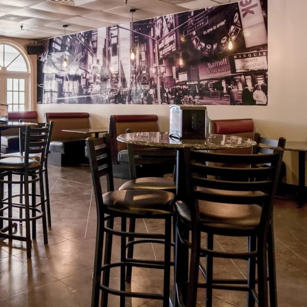 Interior of New York Bagel Company with high-top tables, booths, and a large Times Square mural.
