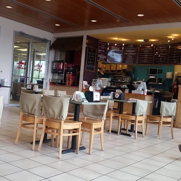 Interior of New York Bagel Company with empty tables and chairs, menu boards, and a service counter.