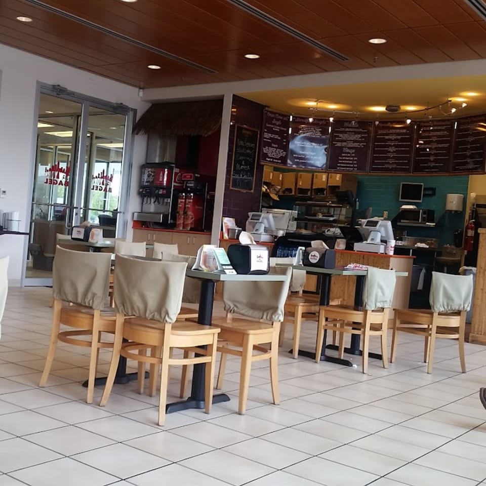Interior of New York Bagel Company with empty tables and chairs, menu boards, and a service counter.