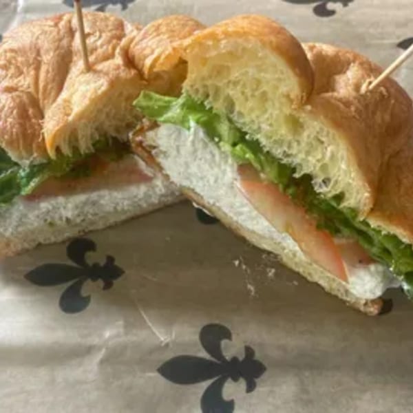 Croissant sandwich with cream cheese, lettuce, and tomato, cut in half on patterned paper.