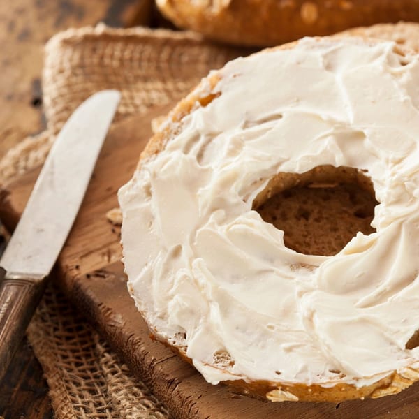 A New York Bagel Company bagel, sliced and generously spread with cream cheese, next to a knife.