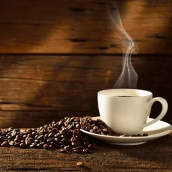 Steaming coffee in a white cup with coffee beans scattered on a rustic wooden surface.